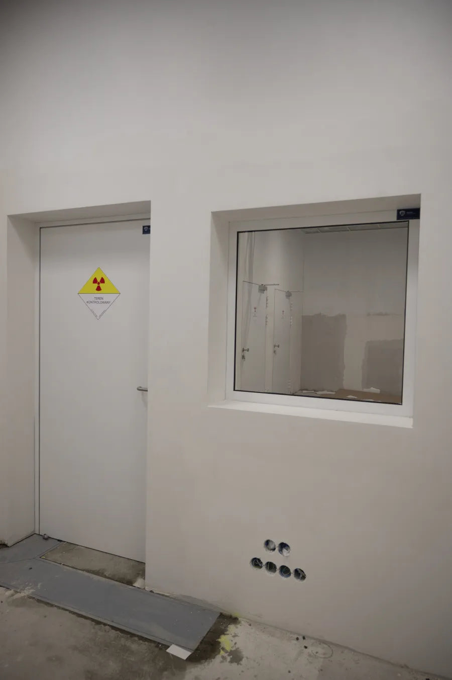 Drzwi RTG ze znakiem terenu kontrolowanego i okno z szybą ołowiową w pracowni RTG
